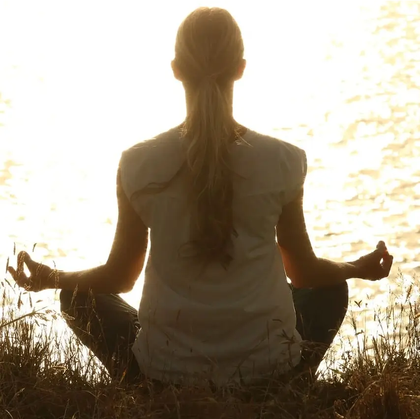 Mujer meditando frente al mar con una bonita puesta de sol